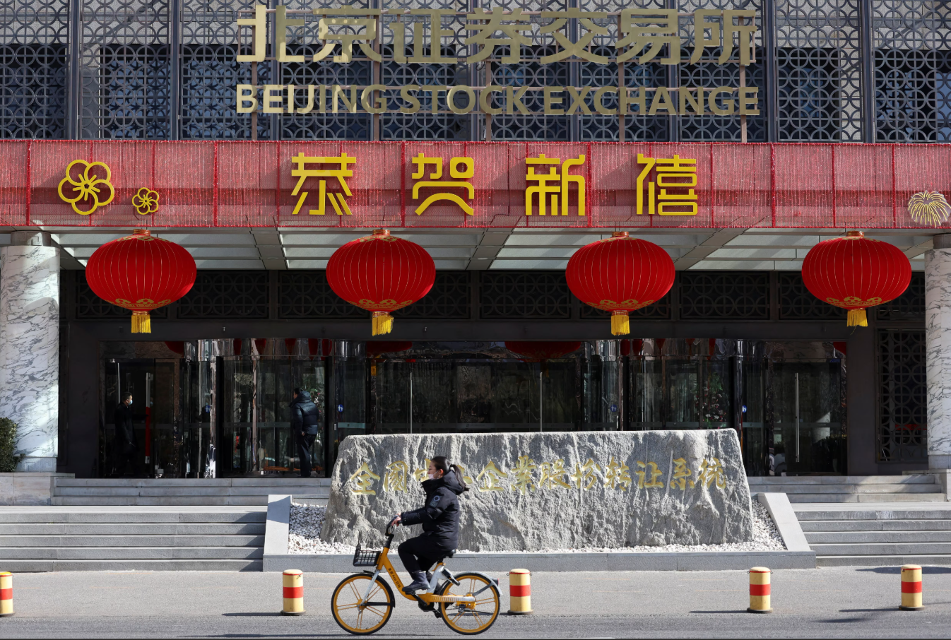 A woman cycles past the Beijing Stock Exchange building adorned with Lunar New Year decorations, on the Financial Street in Beijing, China, Feb. 8, 2024.