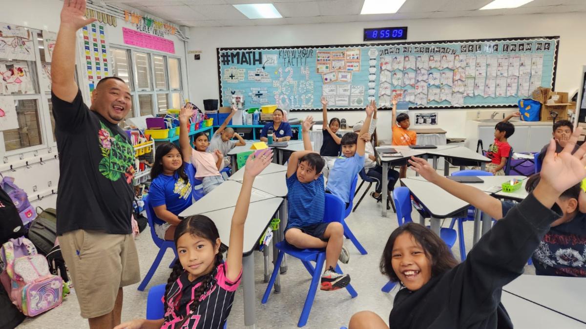 Marianas Visitors Authority Community Projects Coordinator Sherman Santos, left, leads 4th graders at Tinian Elementary School in pledging to be friendly to visitors and help keep their island clean during a presentation at their school in San Jose, Tinian, on Feb. 14, 2025.
