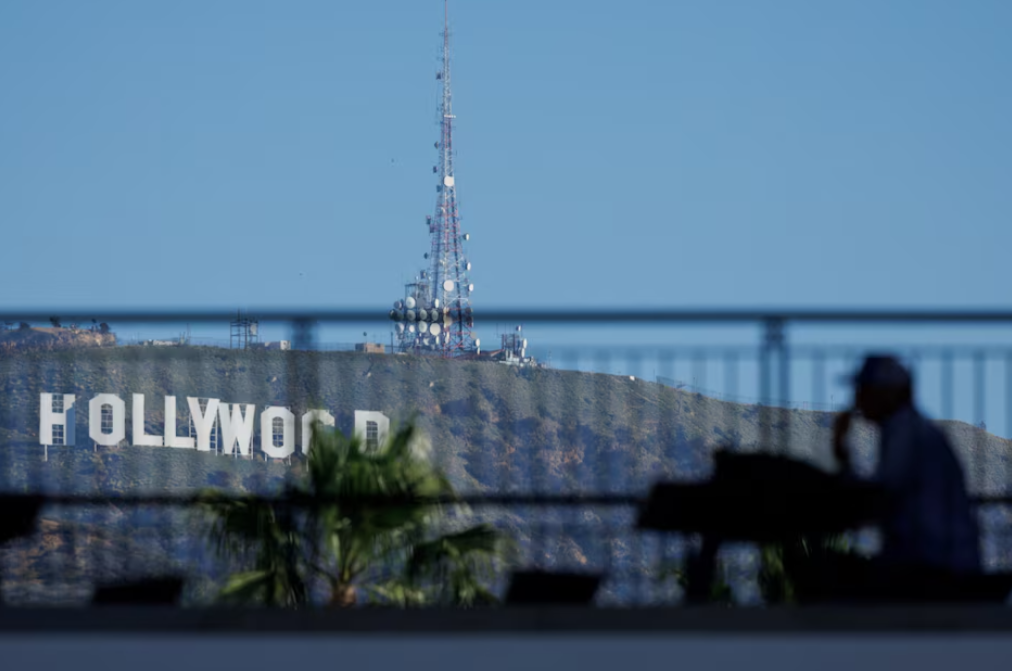 The iconic Hollywood sign is shown behind a person sitting in the shade along Hollywood Blvd as the city prepares to host the 97th Academy Awards in Los Angeles, California, Feb. 25, 2025.