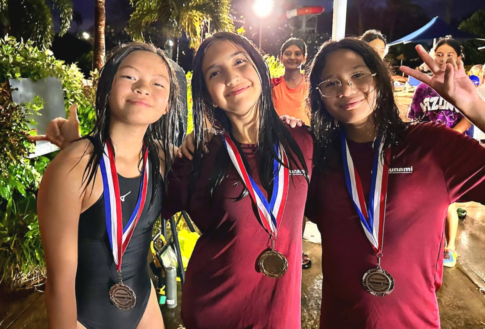 The top three swimmers of the 100m freestyle, 11&12 age group, Sera Guerrero, Catalina Frink, and Gwen Retardo, pose for a photo with their medals.