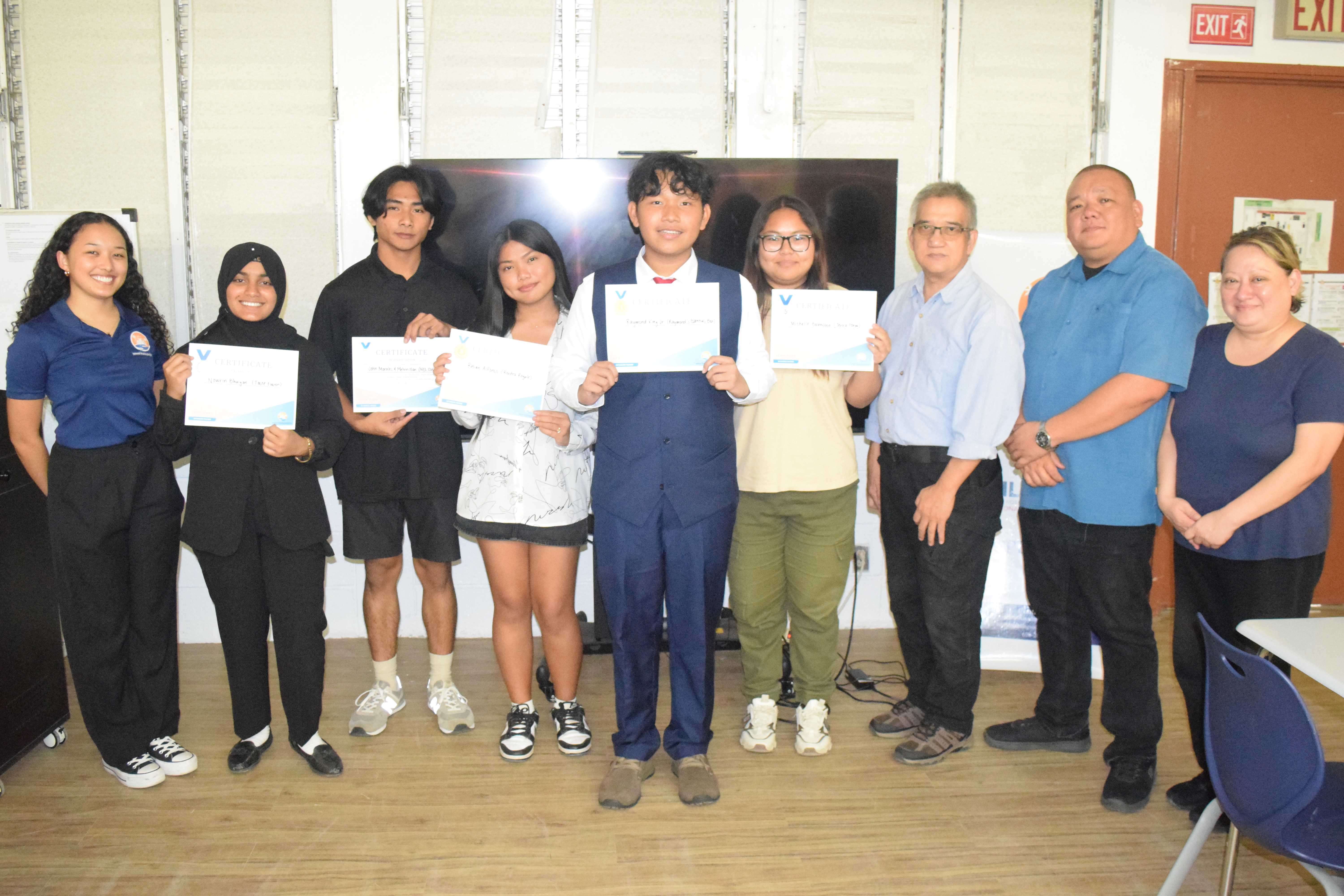 Marianas High School ninth grader Raymond King Jr., center, and other Shark Tank competitors pose for a photo with Public School System Assistant Commissioner for Administrative Services Eric Magofna, second right, PSS Career and Technical Education Director Jessica Taylor, right, and Island Training Solutions instructor Arnel Gruspe in Room C-203 of MHS on Thursday.Photo by Emmanuel T. Erediano