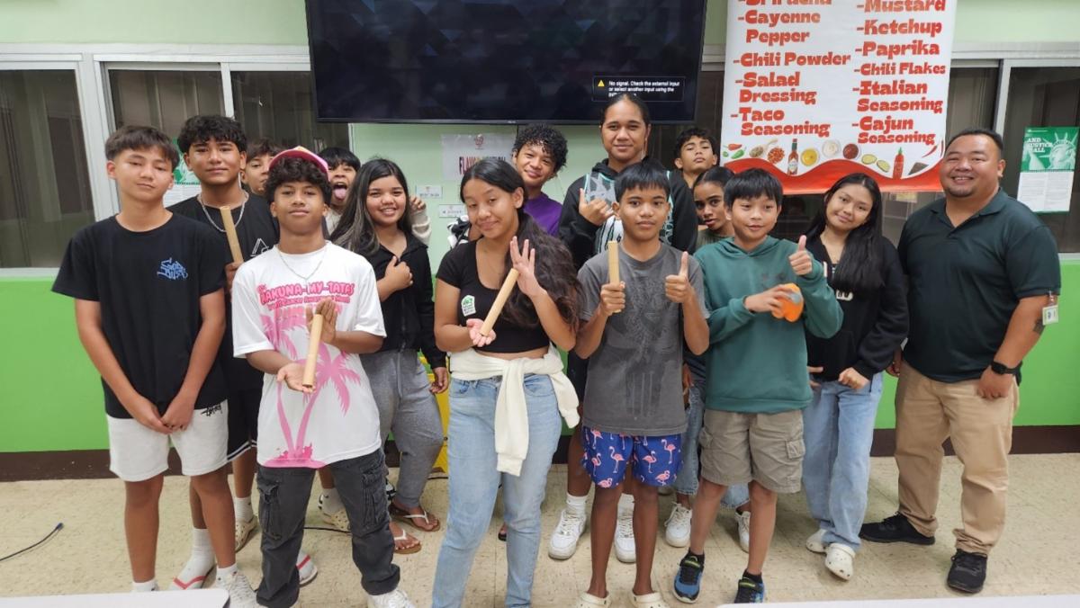 A group of 7th graders of Tanapag Middle School take a commemorative photo with Marianas Visitors Authority Community Projects Coordinator Sherman Santos, right, following the educational outreach of MVA and the Marianas Tourism Education Council at the school on April 21, 2025. Students won Marianas-branded giveaways for sharing what they learned about The Marianas tourism economy and how they can support the industry.MVA photo