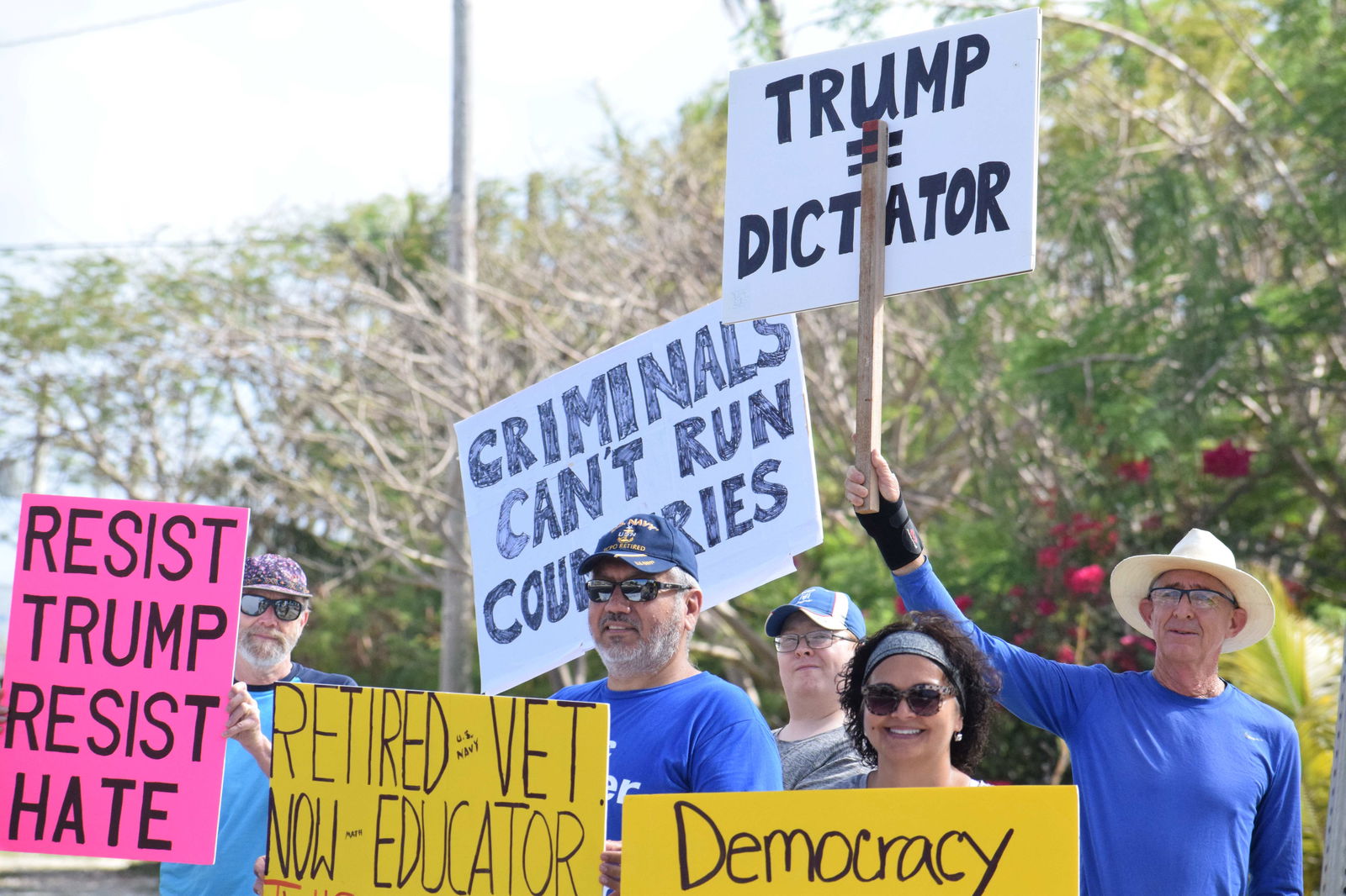 Jeff Race, right, holds a placard that says, “Trump Dictator” as he and about 10 other residents stage a “hands-off” protest on Beach Road in Oleai on Saturday.