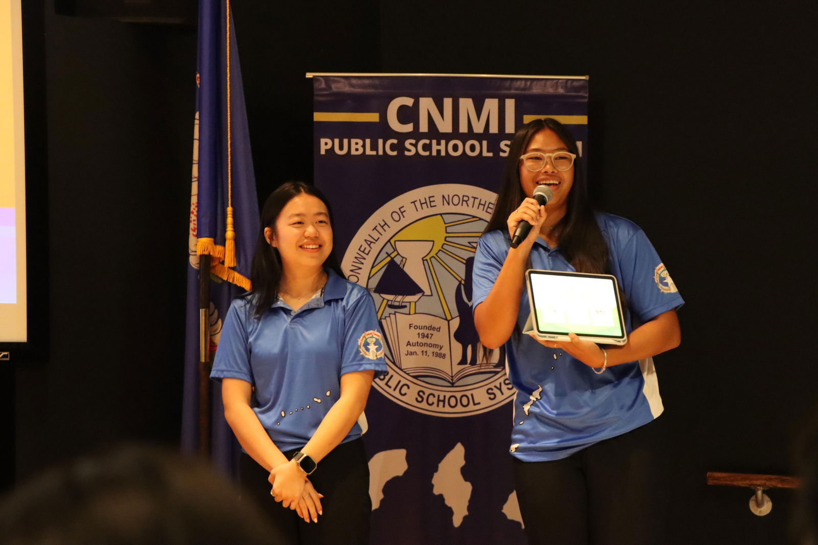 Kelly Zheng of Marianas High School, left, smiles as Mai Peters, right, talks about the winning Congressional App Challenge called “Neni,” which was designed by a team of students that consisted of Peters and Yu Ling Chai of Saipan Southern High School and Zheng and Jedric Aniciete of Marianas High School.