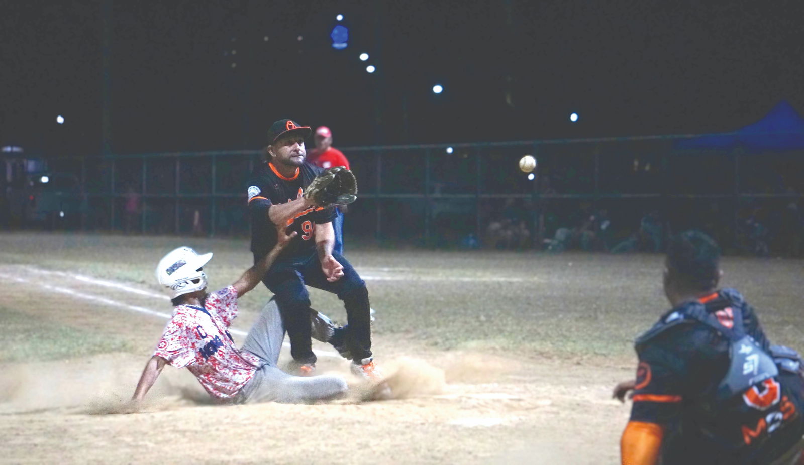 The Orioles’ Bob Coldeen Jr. reaches to catch the ball in a pickoff attempt as the Bears’ Aurel Mendiola slides home to score a run during a Saipan Baseball League game at the Francisco “Tan Ko” Palacios Baseball Field on Wednesday night.Photo by James F. Sablan Jr.