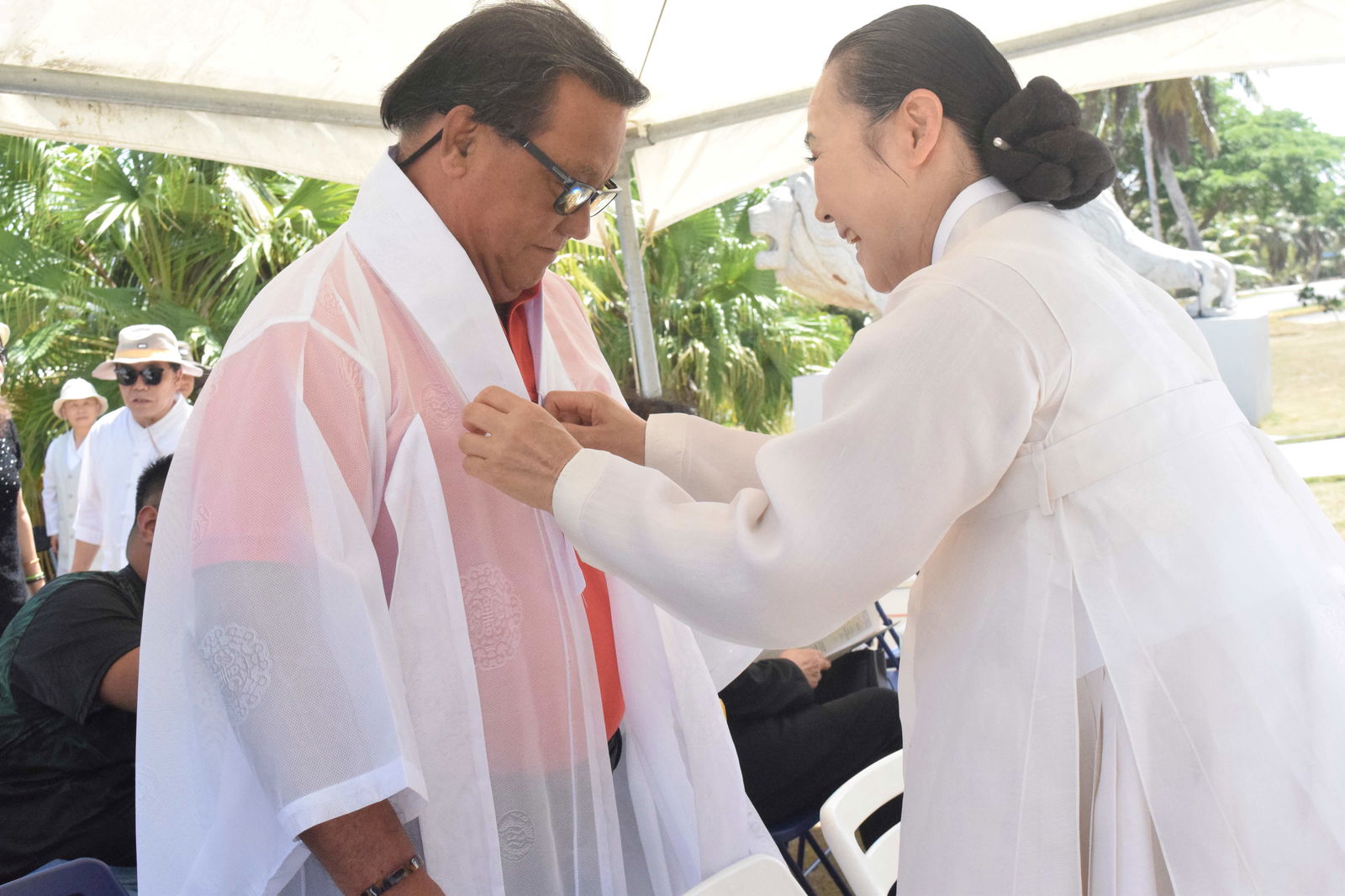A member of the Saipan Dance Research Institute helps Saipan Mayor Ramon Blas “RB” Camacho into traditional Korean attire before the memorial service.
