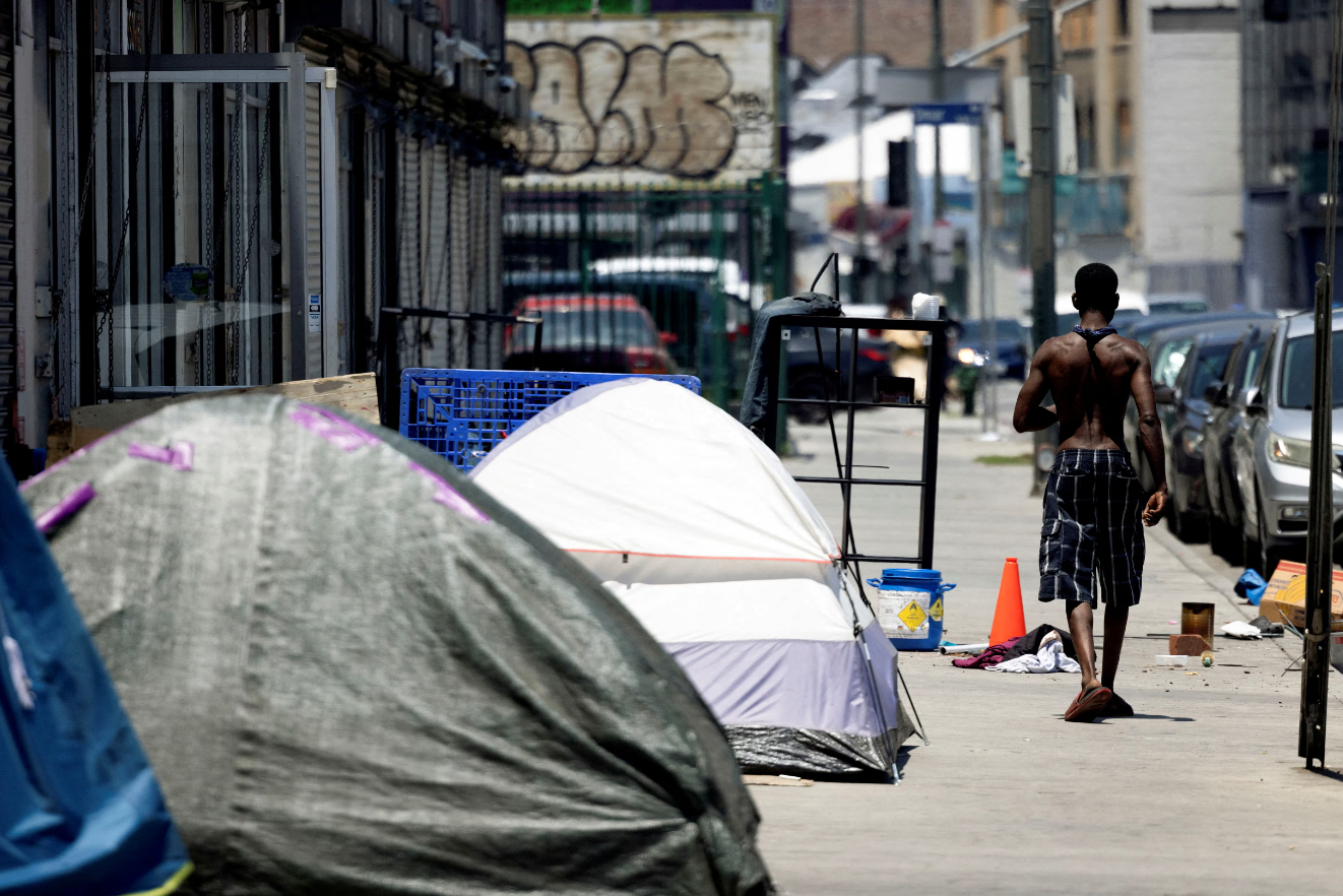 A man experiencing homelessness walks by tents on the sidewalk in Skid Row during hot weather in Los Angeles, California, July 5, 2024.REUTERS
