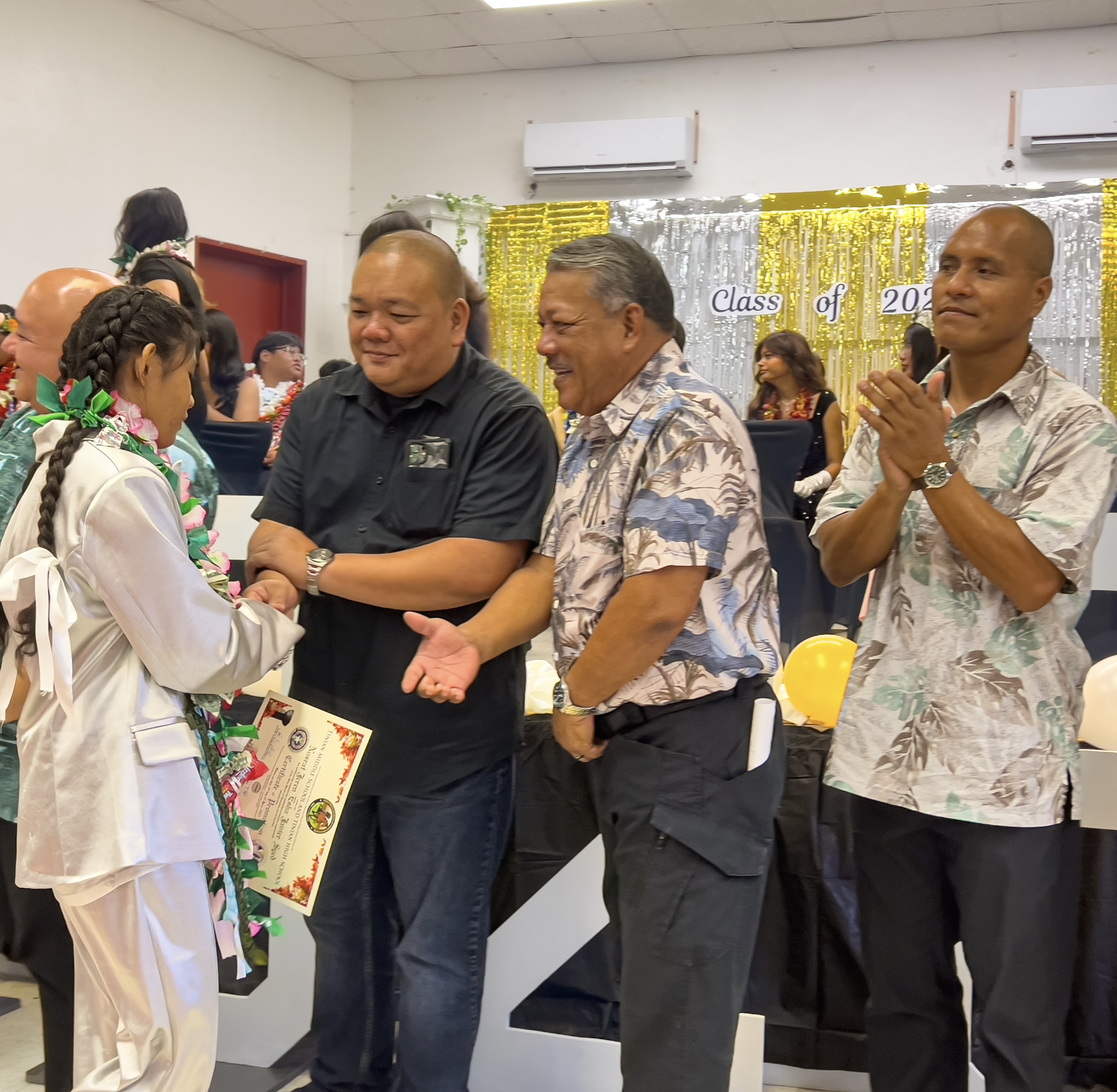 A promoted student is congratulated by Associate Commissioner for Administrative Services Eric Magofna and Tinian Mayor Edwin Aldan as Rota Sen. Ronnie Calvo applauds.