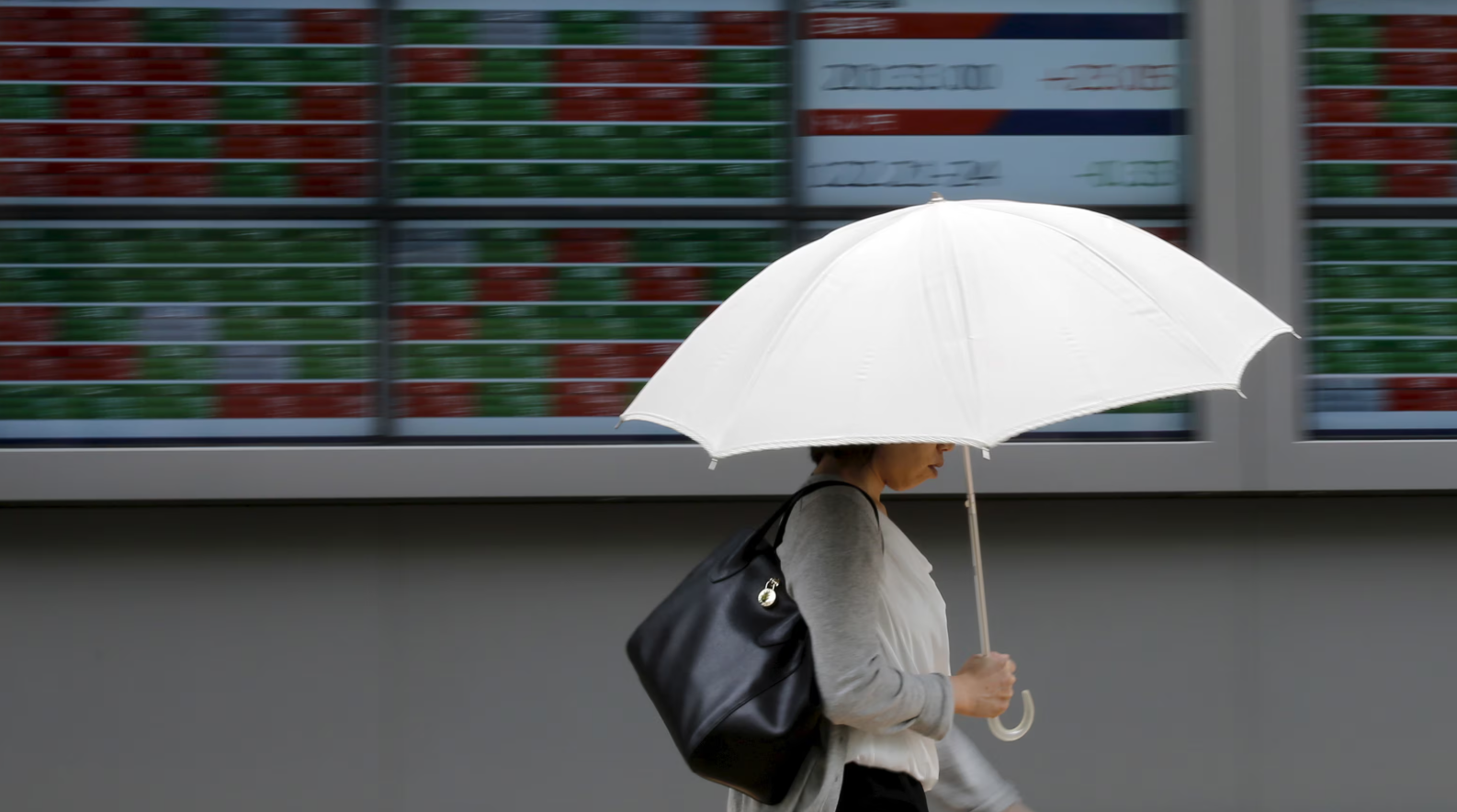 A woman holding a parasol walks past a stock quotation board outside a brokerage in Tokyo, June 30, 2015.REUTERS