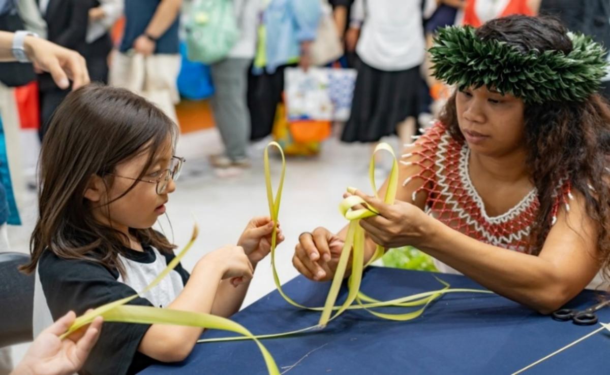 A young attendee of the 40th Seoul International Travel Fair in Seoul, South Korea learns coconut frond weaving from April Repeki, right, at the Marianas Visitors Authority booth.