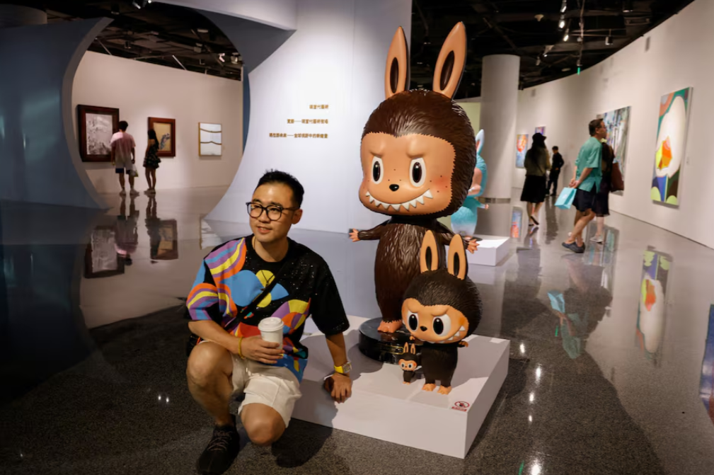 A man poses for pictures next to a life-sized Labubu figurine displayed before an auction in Beijing, China June 6, 2025. The figurine was later sold for 820,000 yuan or about $114,000 at an auction by Yongle International Auction.REUTERS