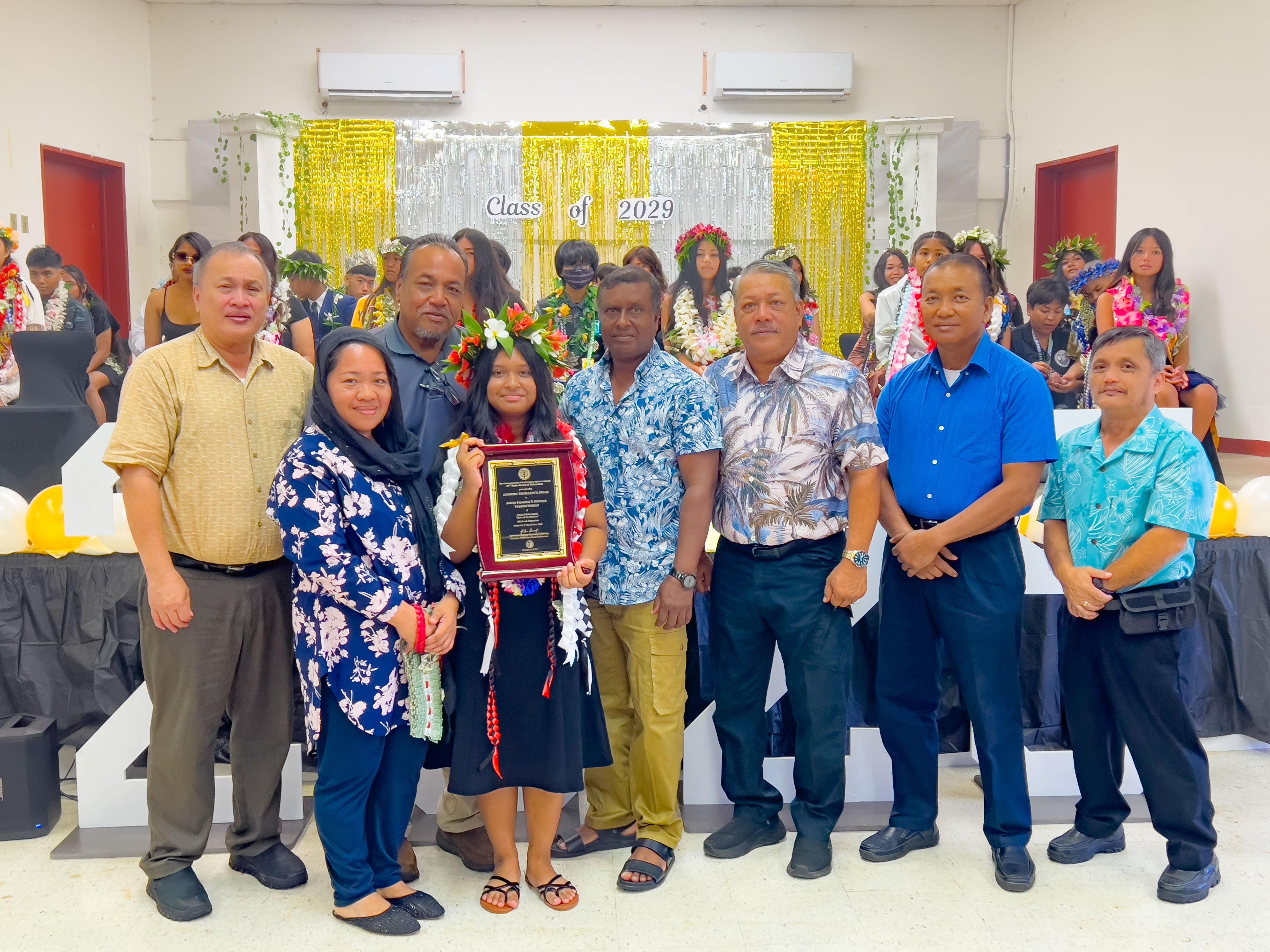Tinian Middle School class valedictorian Amina Fajamida Vera Hossain received the Board of Education Academic Excellence Award from BOE Vice Chairman Anthony DLC Barcinas and BOE Member Andrew L. Orsini. Also in photo are Hossain’s family, Tinian and Aguiguan Mayor Edwin P. Aldan, Tinian Sen. Francsico Cruz, and Tinian Municipal Councilman Estevan P. Cabrera.