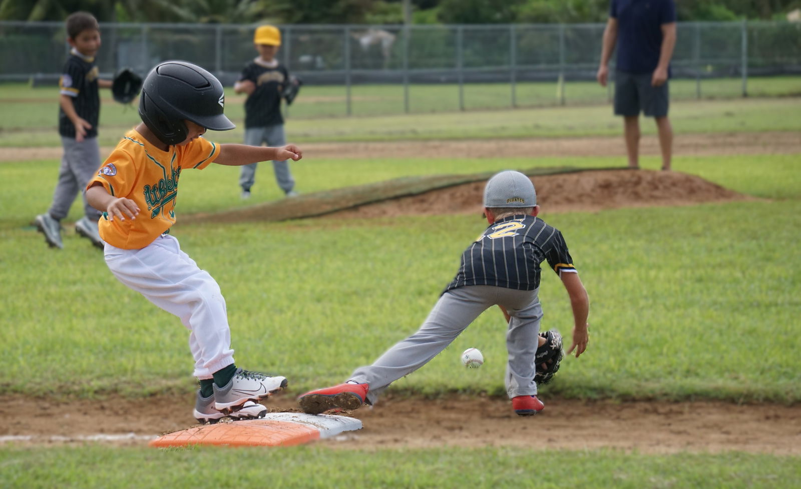 The Athletics' Milo Standish safely reaches first base after beating the pickoff attempt during an opening game against the Pirates in the 2nd Annual Summer T-Ball League 2025 at the Francisco "Tan Ko" Palacios Baseball Field on Sunday.