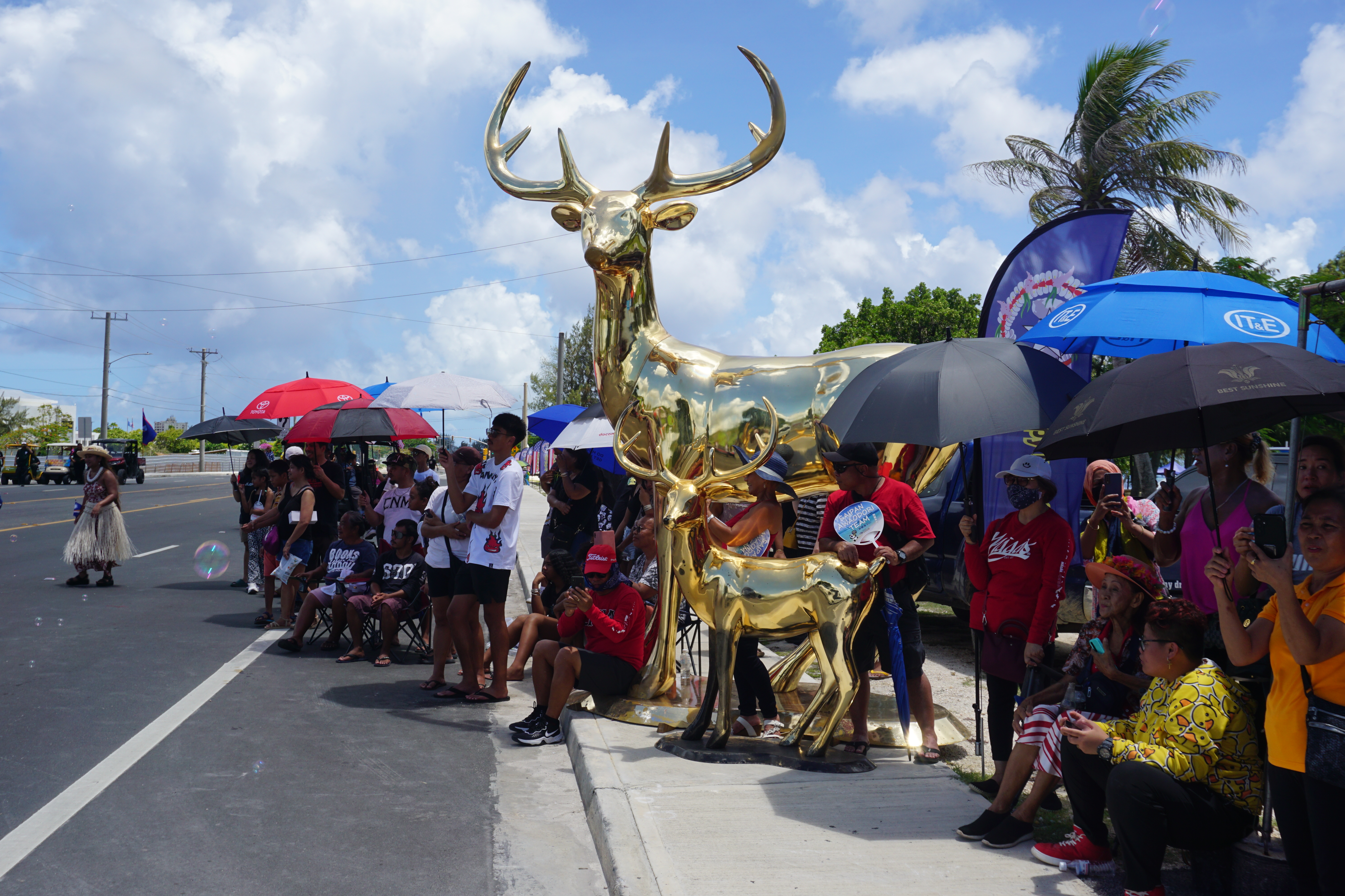 Spectators stand in front of a gold deer decoration near the parade grandstand.