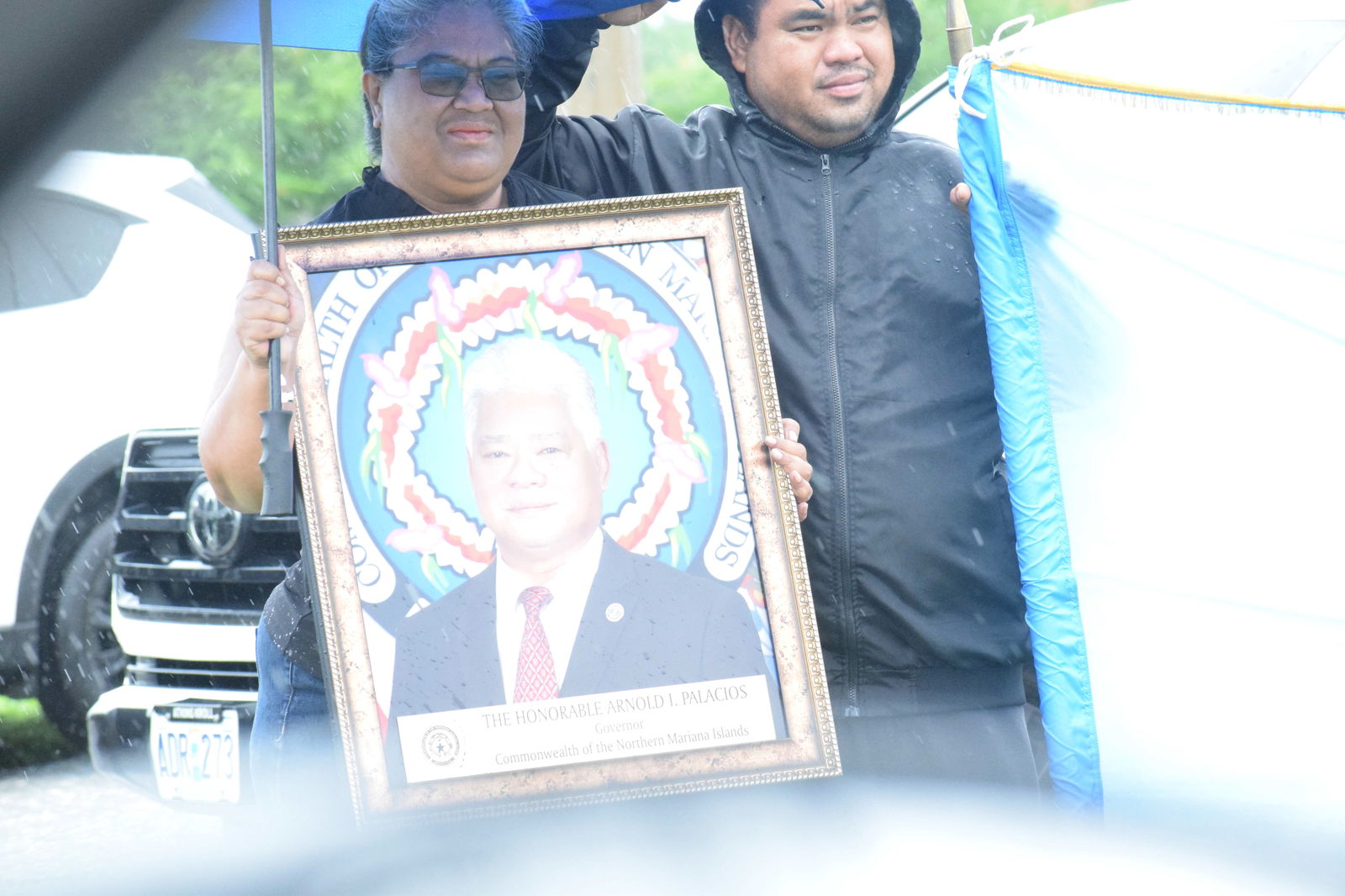 A resident holds up a framed photo of the late Gov. Arnold I. Palacios along the roadside near the airport.