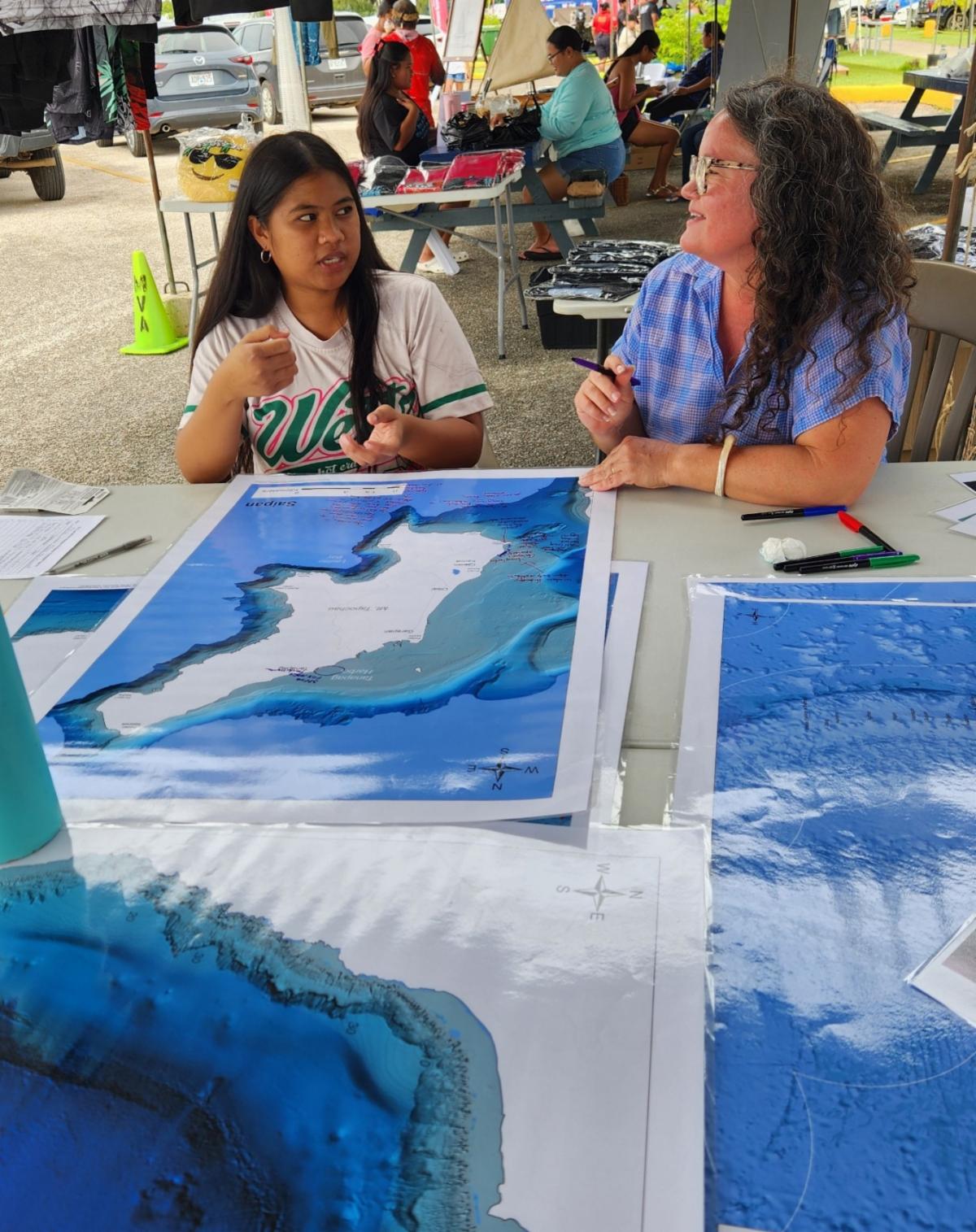 A young festivalgoer shares stories with researcher Dr. Jennifer McKinnon of East Carolina University at the Marianas Maritime Heritage Mapping event during the Saipan International Fishing Tournament festival on July 13, 2025, at Smiling Cove Marina.
