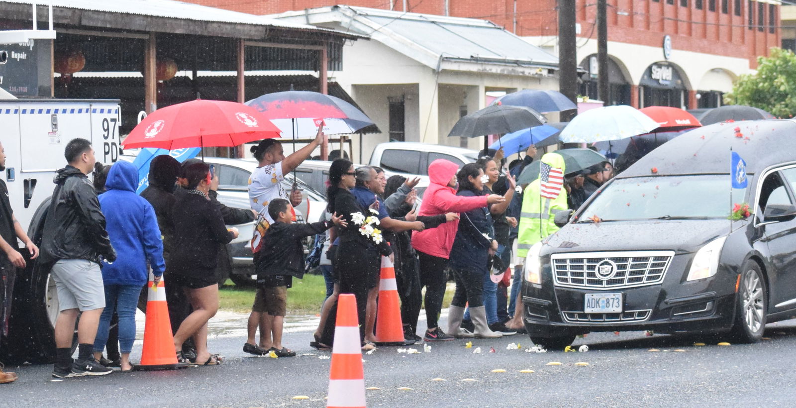 Outside the Commonwealth Utilities Corp. office in Dandan, residents toss plumeria flowers at the hearse carrying the casket of the late Gov. Arnold I. Palacios.
