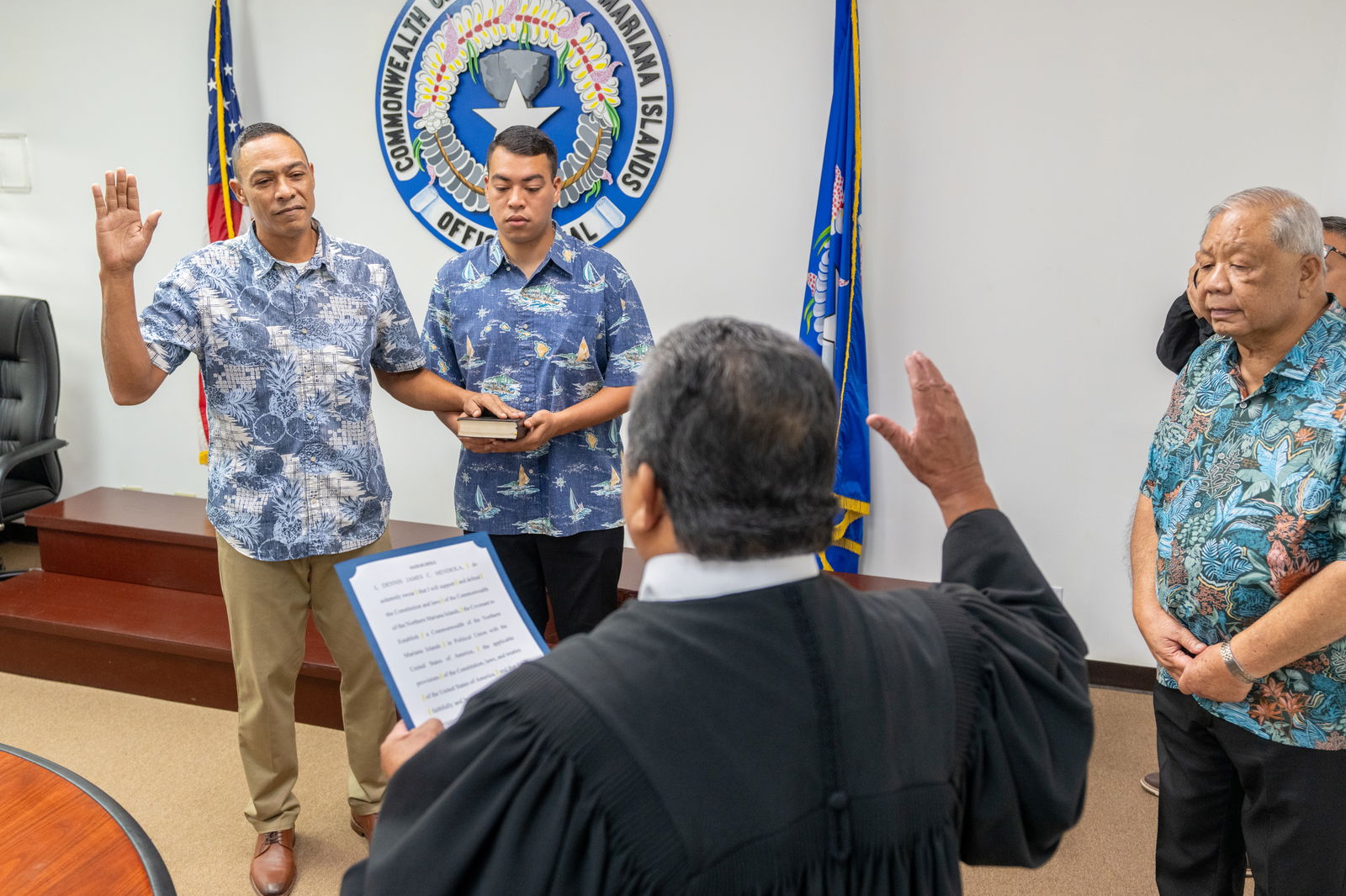 Chief Justice Alexandro Castro, back to the camera, swears in the new lt. governor, Dennis C. Mendiola, while the newly sworn in governor, David M. Apatang, looks on.